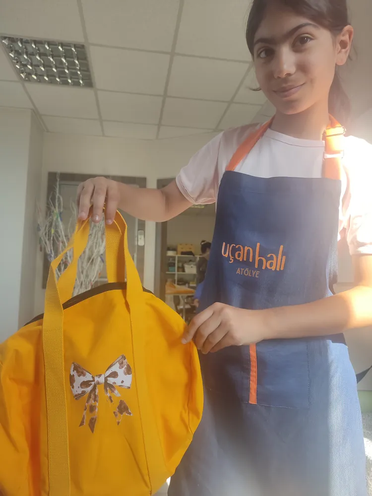 Çocuk atölyesinde fiyonk desenli çantasını gösteren katılımcı